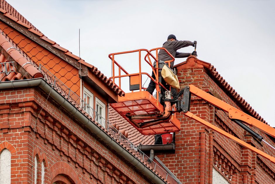 Roofer in a cherry picker working on the tiled roof of a red-brick building